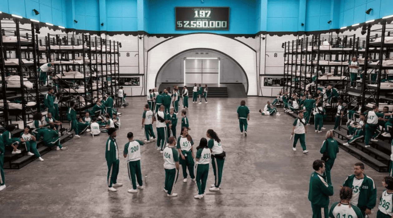 A group of people dressed in identical tracksuits gather in a room with tall bunk beds lining the walls in this image by Studio Lambert.