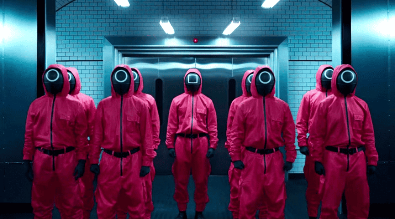  A line of people dressed in red suits and masks stand creepily in front of an industrial background in this photo by Studio Lambert.