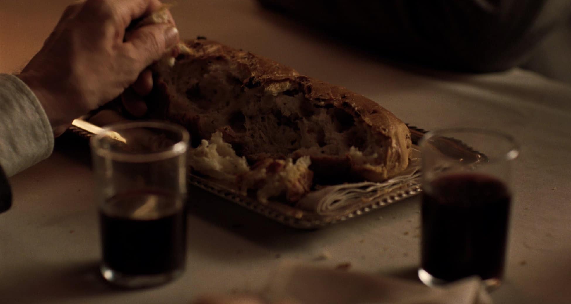 A man tears a piece off a loaf of bread with red wine in his glass in this image from Tribeca Productions.