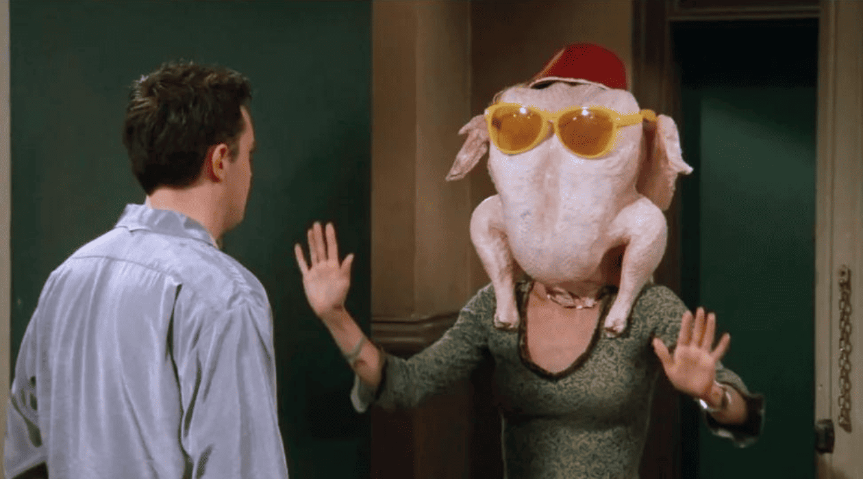 A man stands at his open door looking at a woman wearing a raw turkey over her head in this image from Bright/Kauffman/Crane Productions.