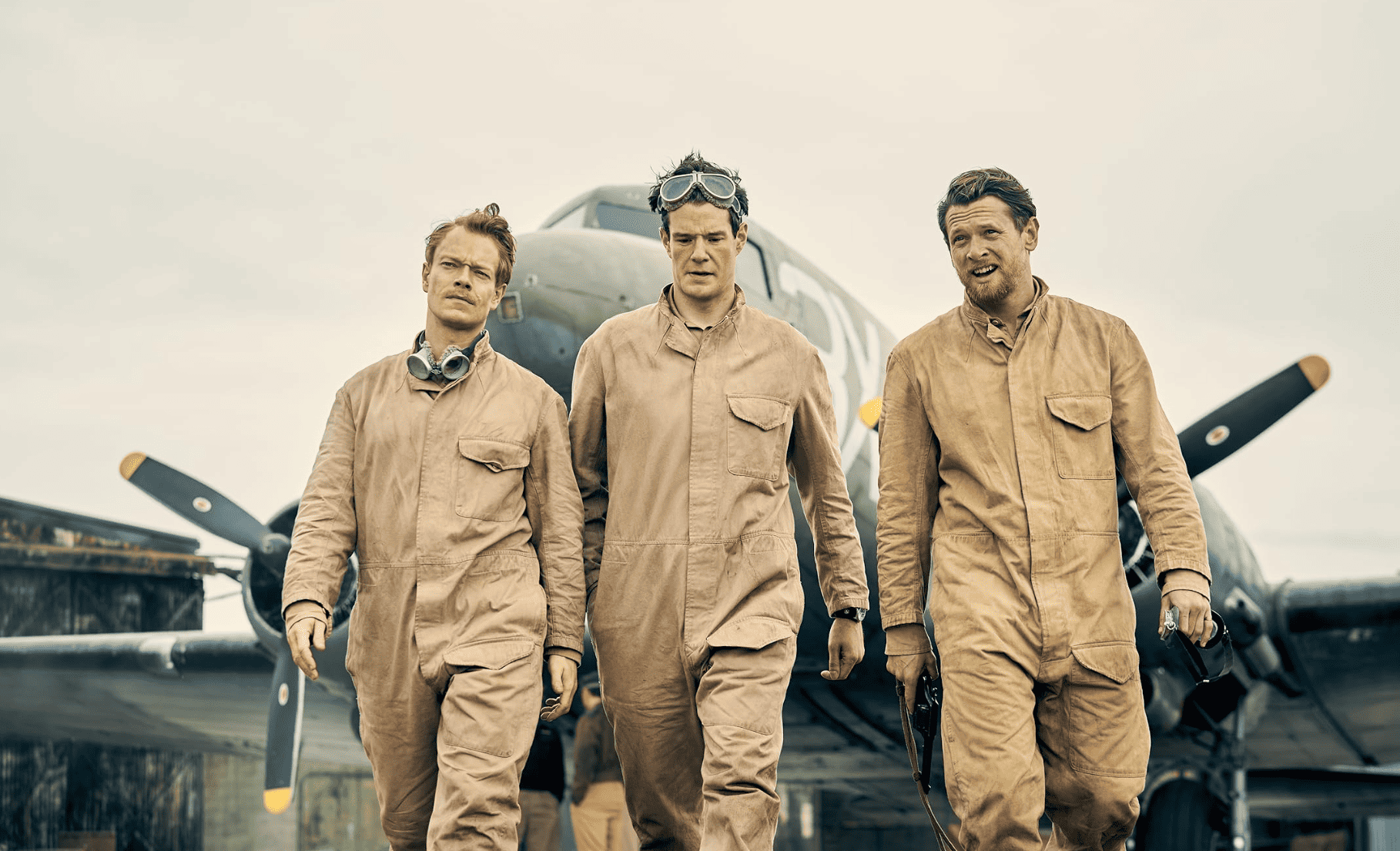 Three men in sky-diving suits walk by a military plane in this image from Kudos. 
