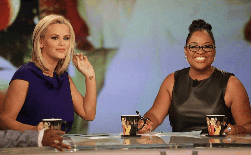 Two women seated at a table with mugs on the set in this image from American Broadcasting Company.