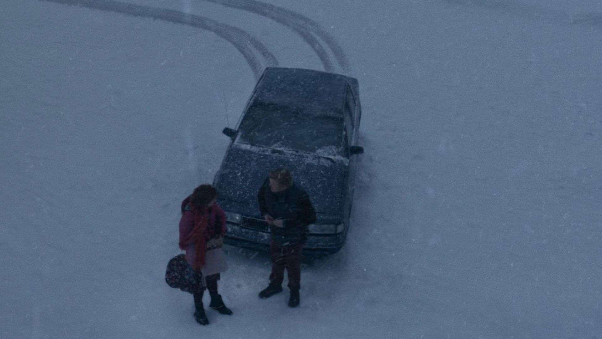 Two people stand in the snow next to a car in this image from Likely Story.