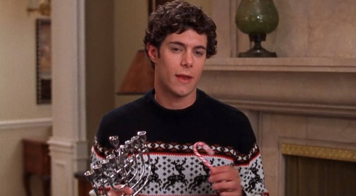 A man holds a menorah and a candy cane in this photo from Warner Bros. Television.