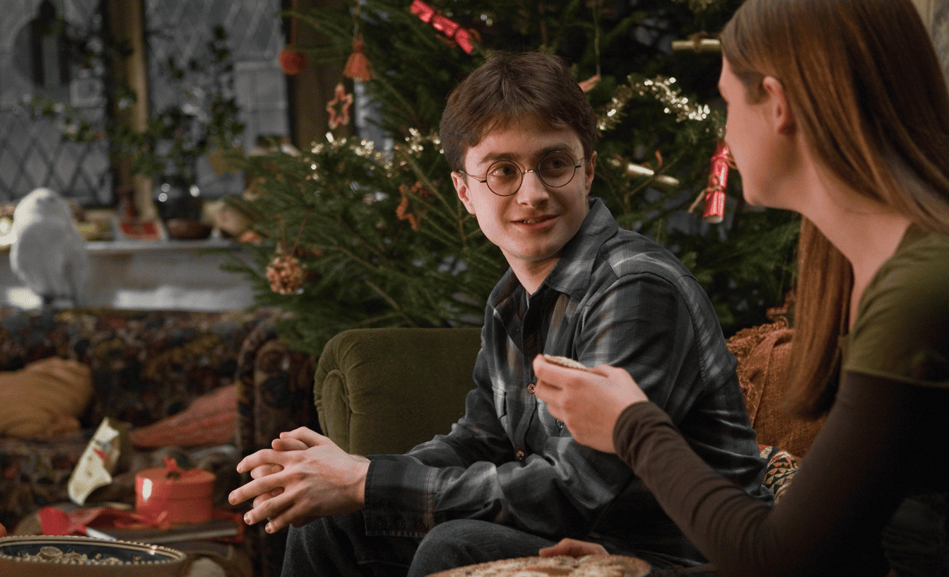 A girl offers a pastry to the boy sitting next to her on a couch with a Christmas tree in the background in this image from Warner Bros. Pictures.