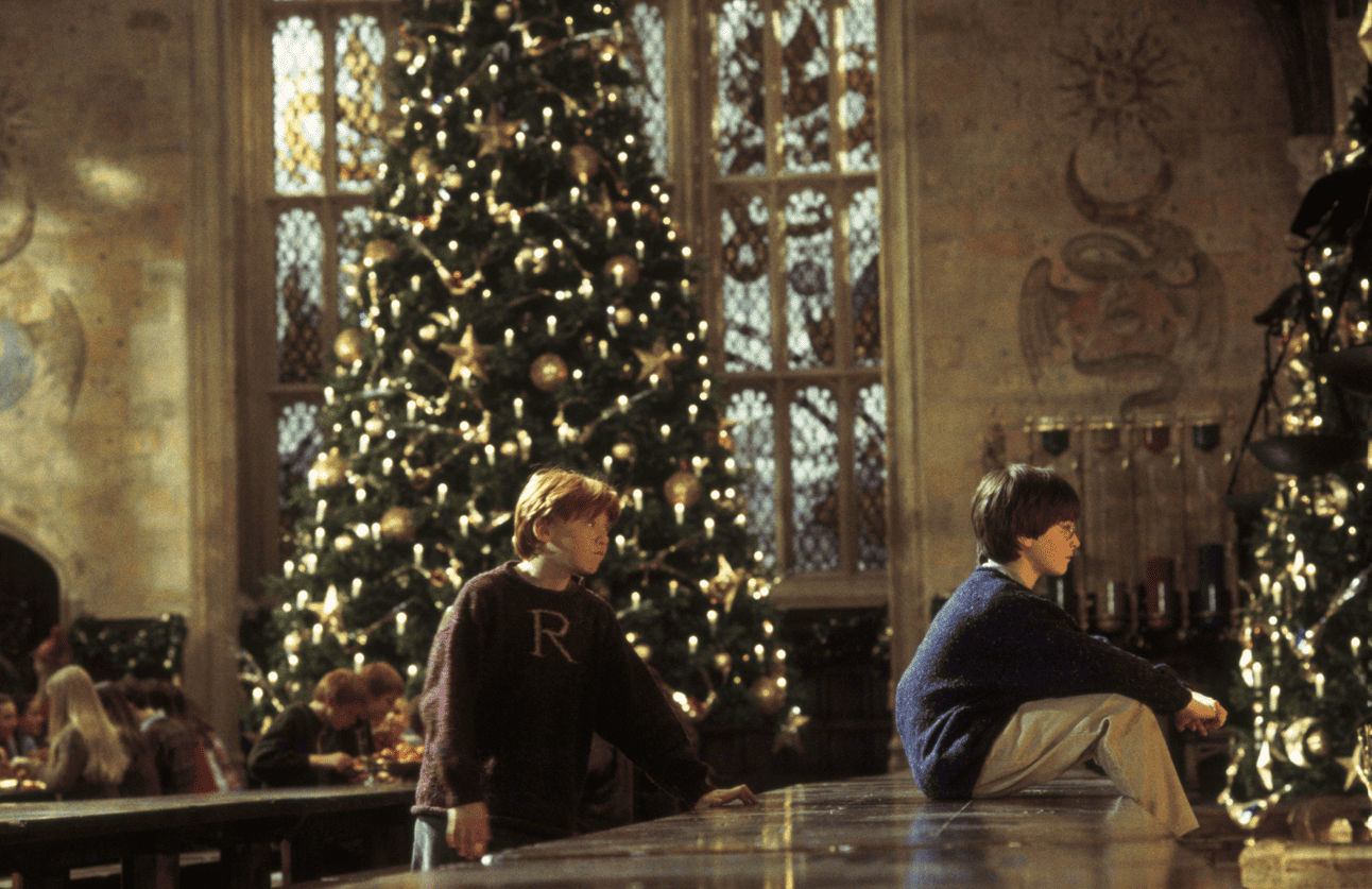 A young boy approaches another from behind as he sits by a Christmas tree in this image from Warner Bros. Pictures.