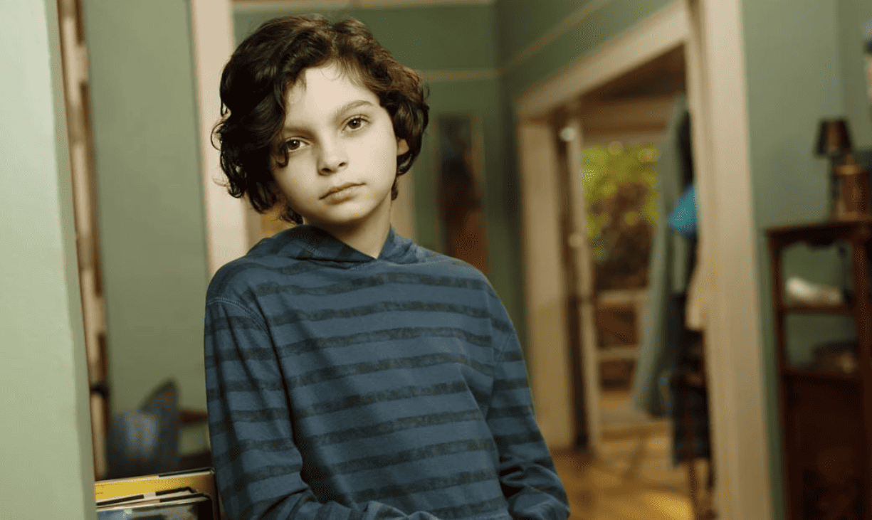 A young boy stands in a hallway in his house, looking ahead, in this image from True Jack Productions.