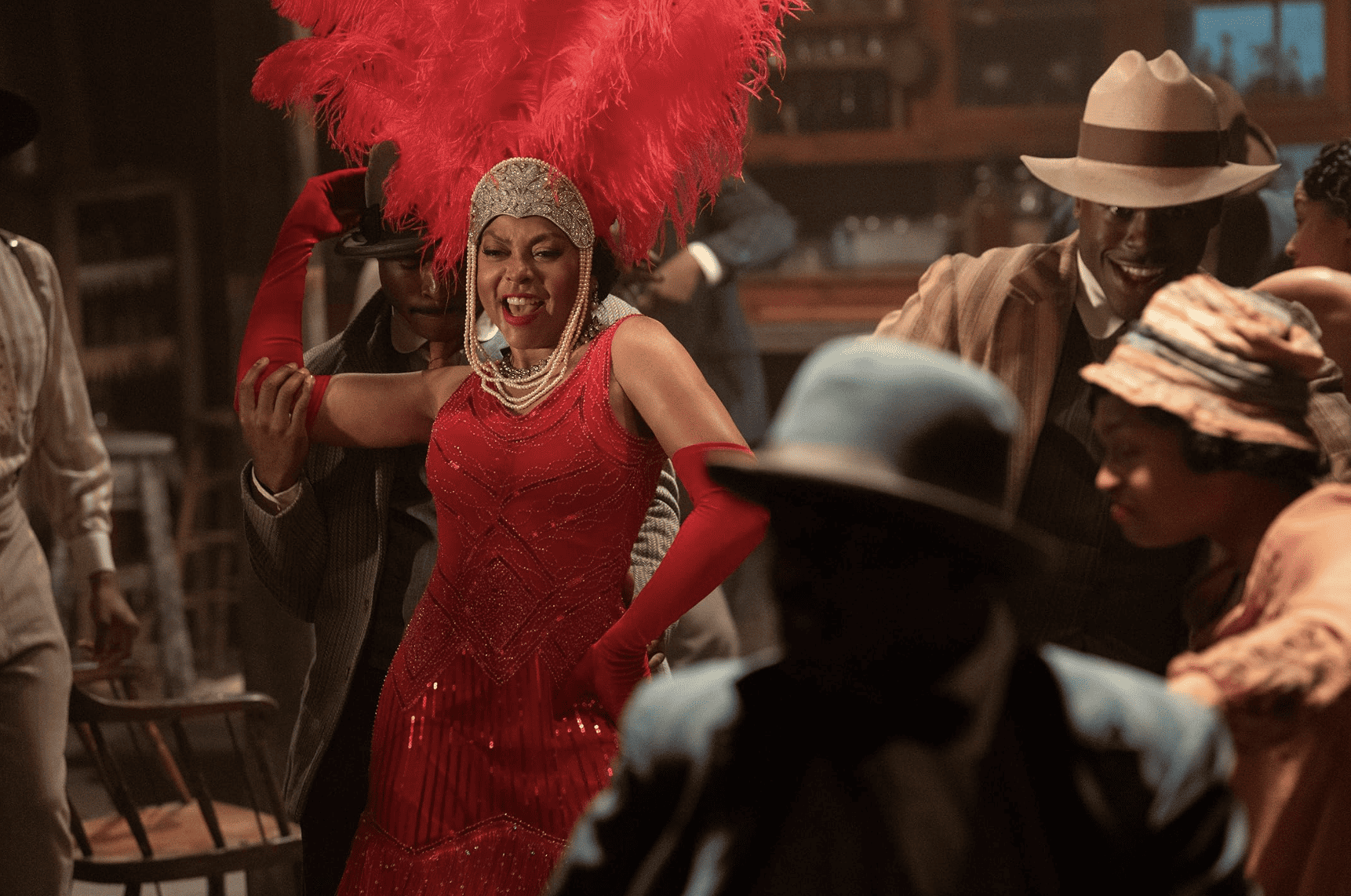 A woman in a red gown and red feather headdress sings and dances in a bar in this image from Amblin Entertainment. 