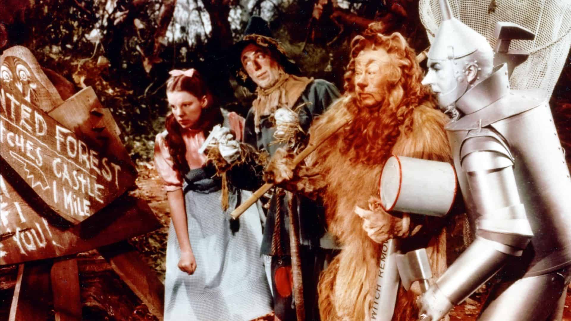 A girl, a scarecrow, a lion, and a tin man read signs for a haunted forest in this image from Metro-Goldwyn-Mayer.