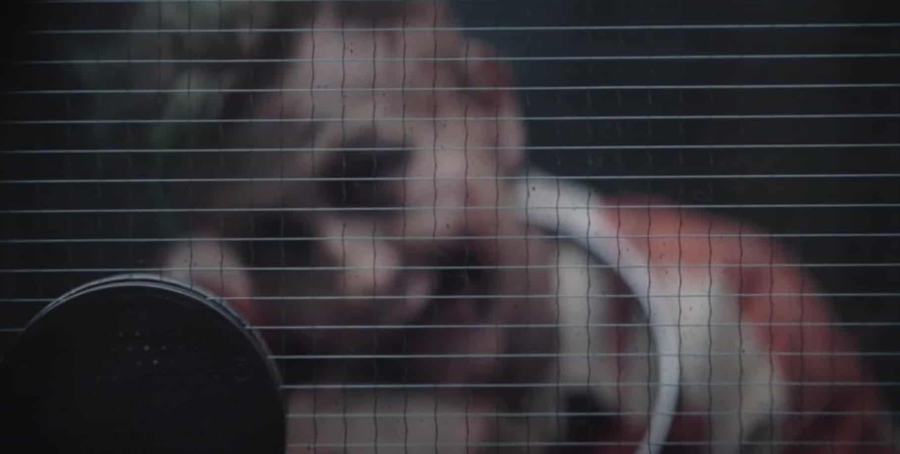 A scarred man is seen behind prison glass in this image from Warner Bros. Pictures.