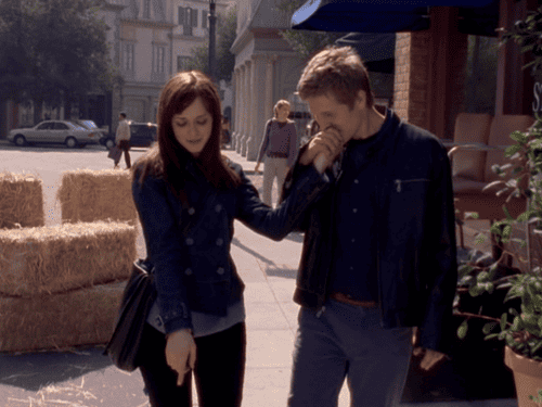 A girl points at something on the ground while her boyfriend kisses her hand in this image from Warner Bros. Television.