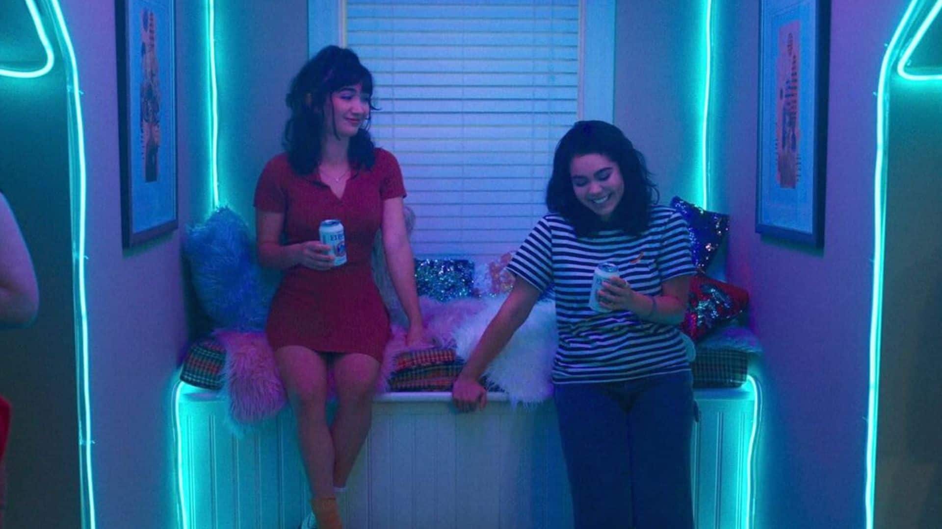 Two young women holding beers in a room with neon lights in this image from Animal Pictures.