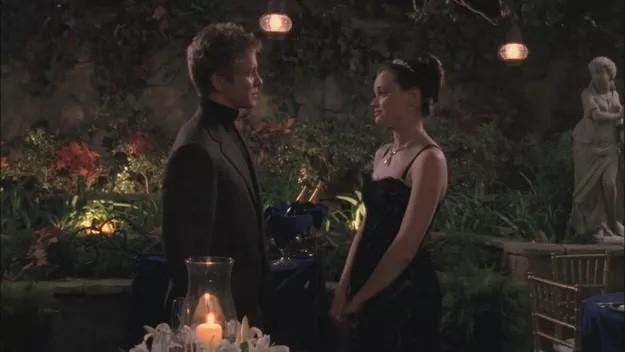 A girl and boy stand in a candlelit garden in this image from Warner Bros. Television.