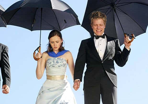  A man and woman, both formally dressed and holding open umbrellas, stare downward in this image from Warner Bros. Television. 