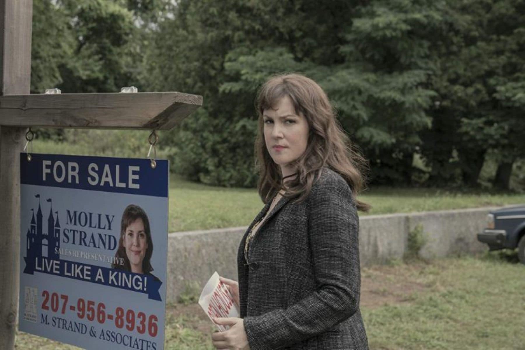A woman adjusts a "for sale" sign in this photo by Warner Bros. Television.