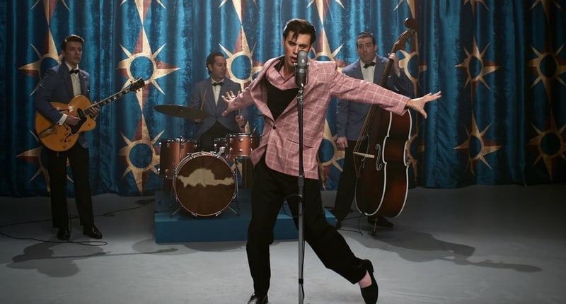 A man on stage performs in front of his band in this image from Warner Bros. Pictures.