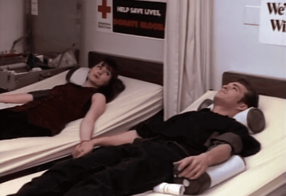 A couple holds hands while lying down to donate blood in this image from Spelling Television.