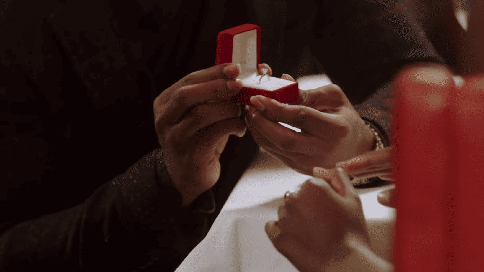 A man’s hand holds an open engagement ring box in this image from Fuqua Films.