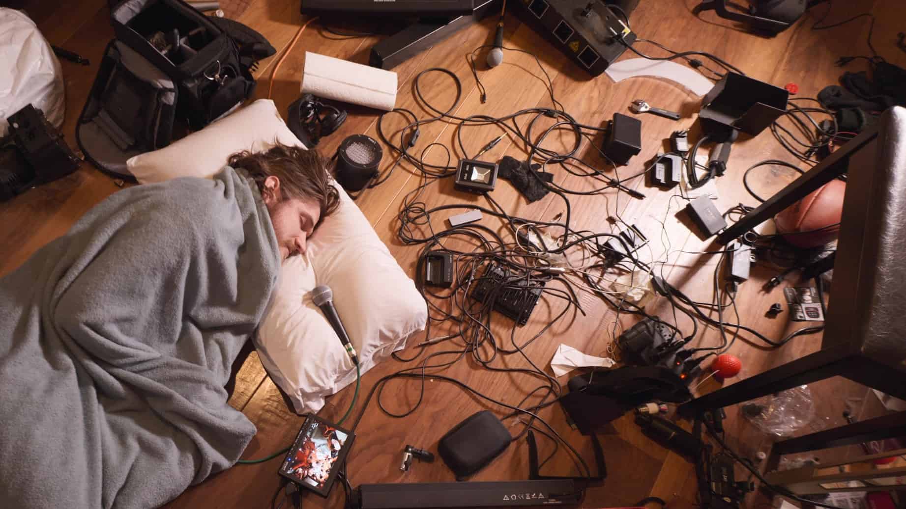 A man sleeps on the floor surrounded by recording equipment in this image from Attic Bedroom.