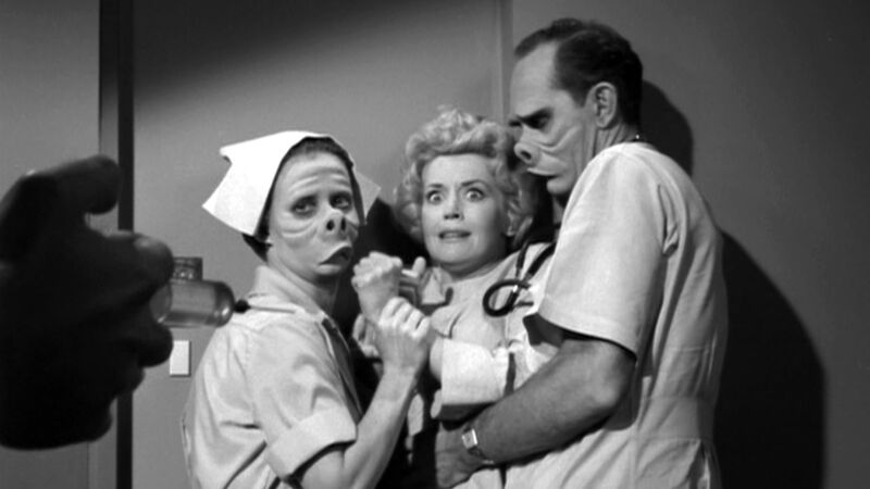 A piglike nurse and doctor hold back a pretty woman while a hand holding a syringe approaches her in this image from Cayuga Productions.