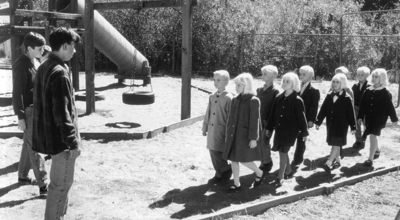 A group of children in matching outfits and haircuts walk through a playground in this image from Alphaville Films.