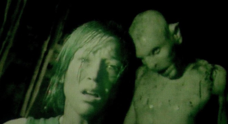 A woman looks through a night-vision camera to see a creature behind her in this image from Celador Films.
