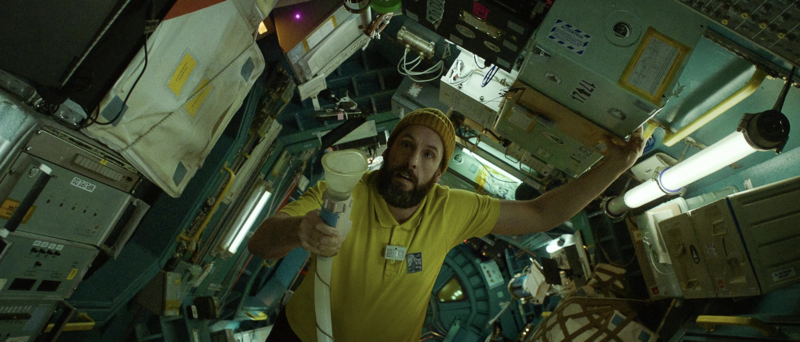 A man in a yellow polo shirt drifts in zero gravity, holding a tube in this image from Free Association.