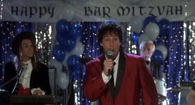 A man in a red suit sings on a stage at a bar mitzvah in this image from New Line Cinema.