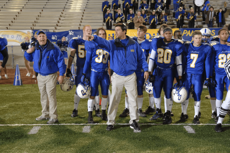 A high school football coach yells toward the field with his team in the background in this image from Universal Television.