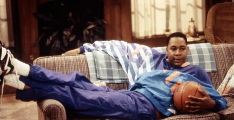 A man lies on a couch holding a basketball while watching TV in this image from Jeff Franklin Productions.