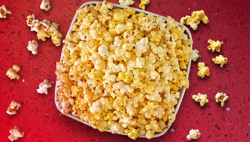 An overflowing popcorn bucket on a red countertop in this image from AMC.