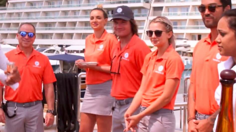 A group of people in orange polos stand on a boat deck in this image from 51 Minds Entertainment.