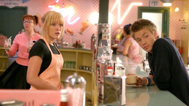 A girl in a pink apron serves a boy her age from behind a bar in a diner in this image from Dylan Sellers Productions. 