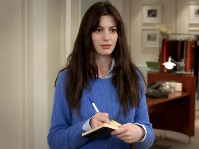 A woman in an ill-fitting blue sweater stands with a notepad and pen in this image from Fox 2000 Pictures.