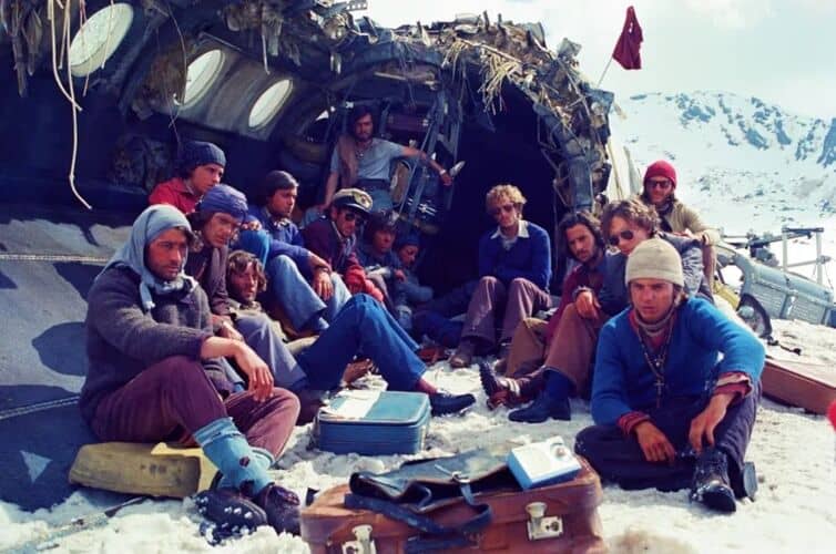A group of men sits in the snow next to the wreckage of a plane crash in this photo by Misión de Audaces Films.