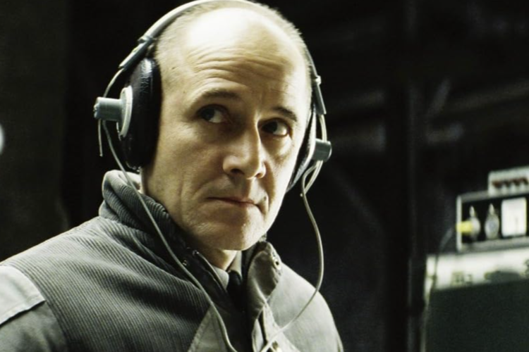 A man wearing headphones with a serious expression intently monitors audio equipment in a dimly lit room in this image from Wiedemann & Berg Film Production.