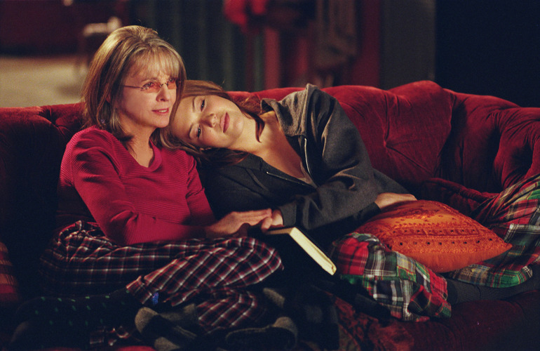 A mother and adult daughter cuddle in PJs on a couch in this image from Gold Circle Films.