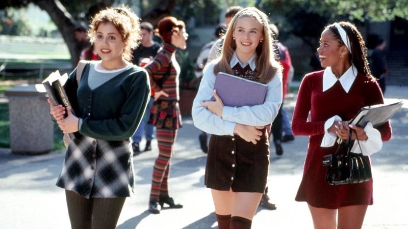 Three teenage girls holding books and binders walk in a sunny school courtyard in this image from Paramount Pictures. 