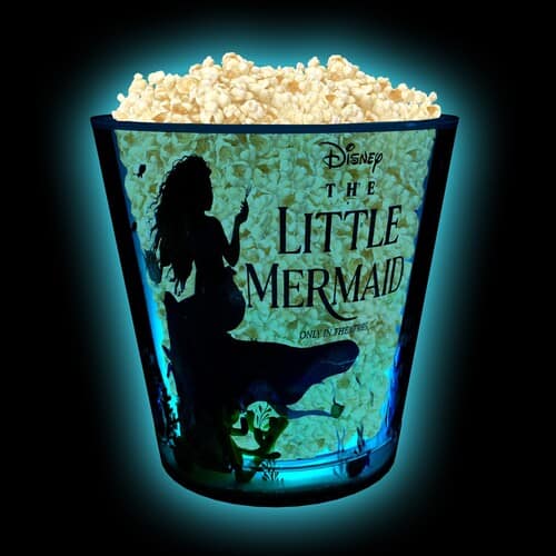 A dark background showing the clear siding of a “Little Mermaid” bucket filled with popcorn in this image from AMC.