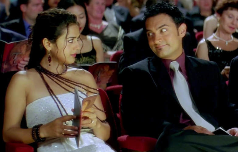 A man in a suit exchanges a playful glance with a woman in a sparkling dress at a formal event, surrounded by an attentive audience in this image from Excel Entertainment.