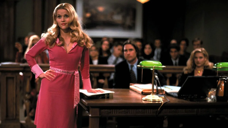 A woman dressed in all pink stands in a courtroom with a full audience in this image from Metro-Goldwyn-Meyer. 