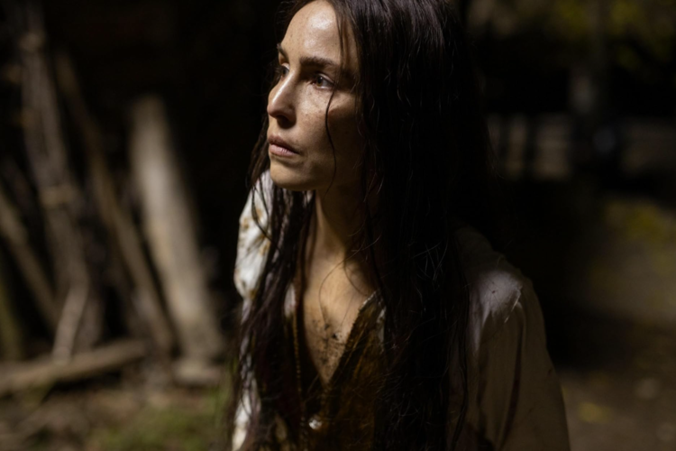 A woman with long, damp hair and a pensive expression stands in a dark, rustic setting, evoking a sense of resilience in this image from Causeway Films.