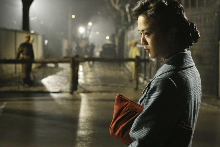 A young woman in a blue checkered coat with a red clutch stands contemplatively on a foggy, lamp-lit street at night in this image from Haishang Films.