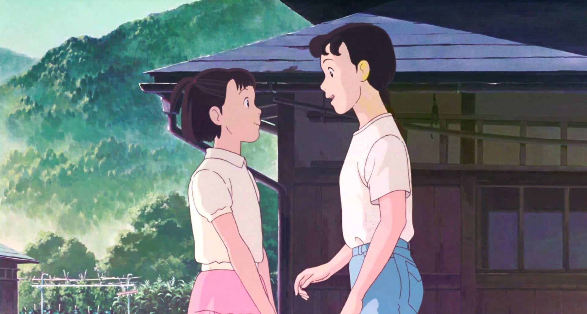 An animated girl and boy stand in front of a mountain home in this image from Studio Ghibli.