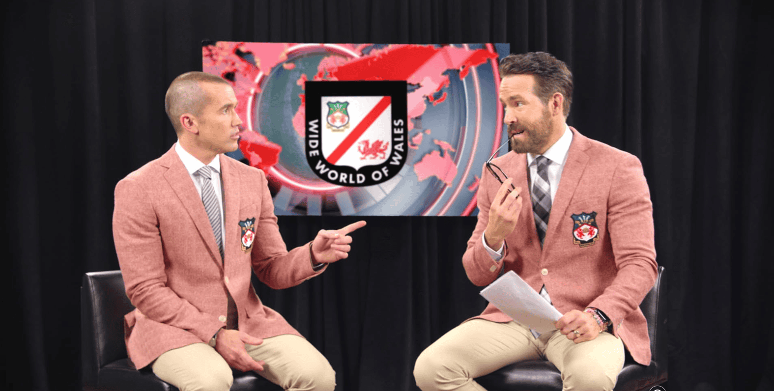 Two men in blazers talk in front of a TV in this episode from Boardwalk Pictures. 
