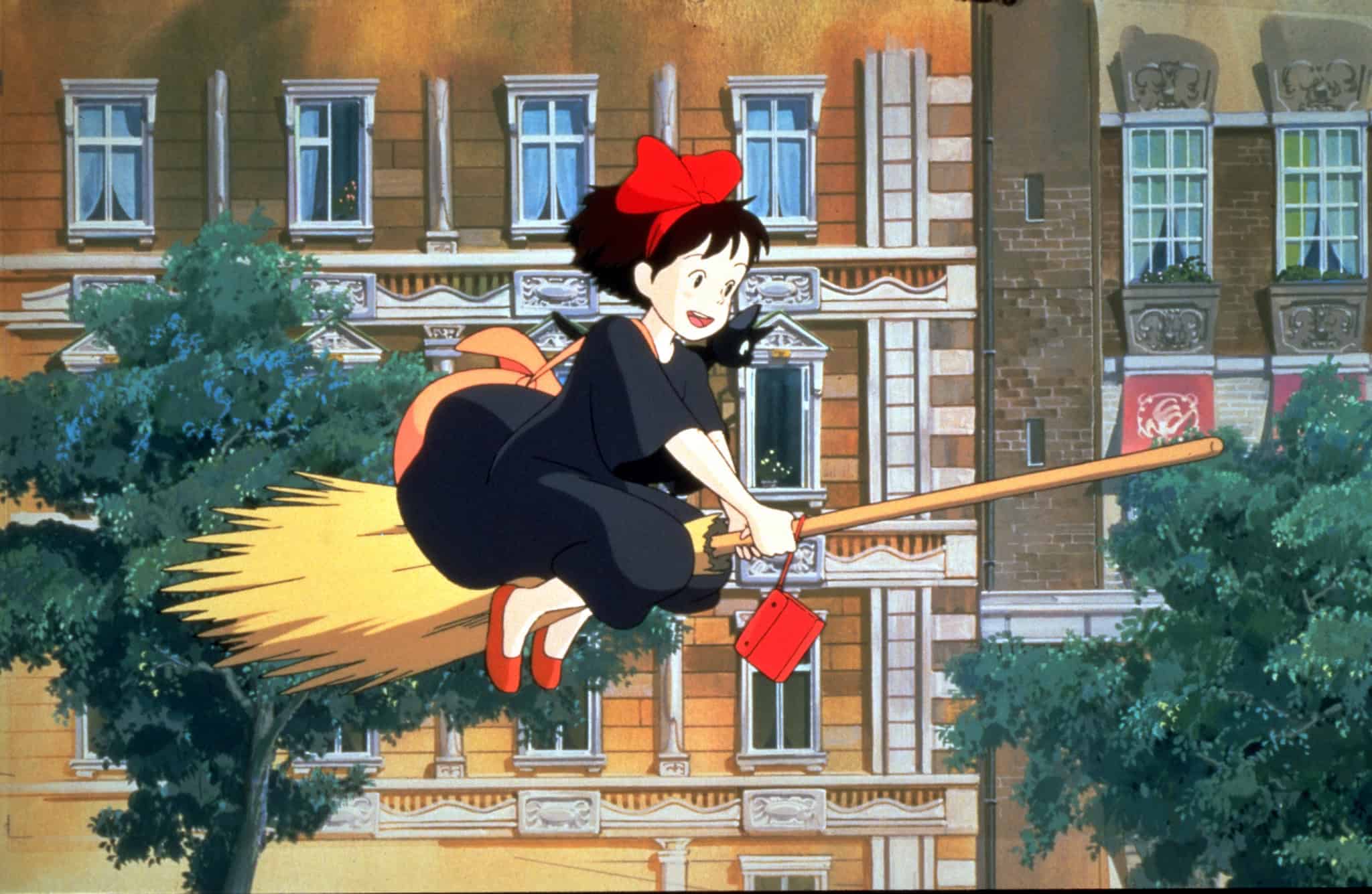 An animated young witch rides through the city on a broom in this image from Studio Ghibli.